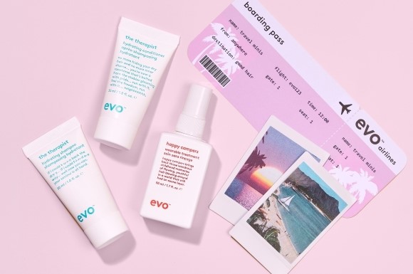 flatlay with evo travel-size products, holiday polaroids and an evo airplane ticket on a pink background